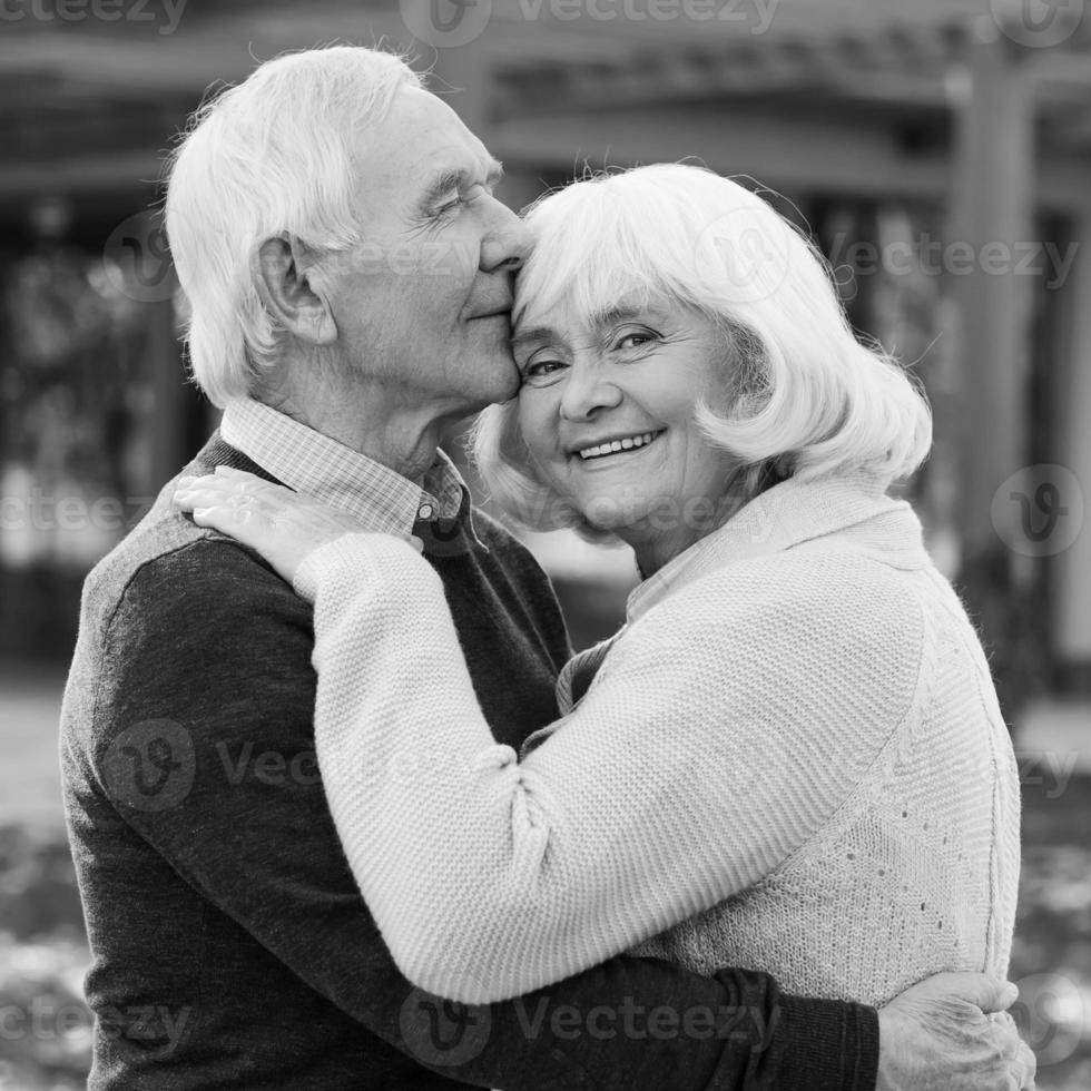 Portrait of endless love. Black and white portrait of happy senior couple bonding to each other and smiling while standing outdoors and in front of their house photo