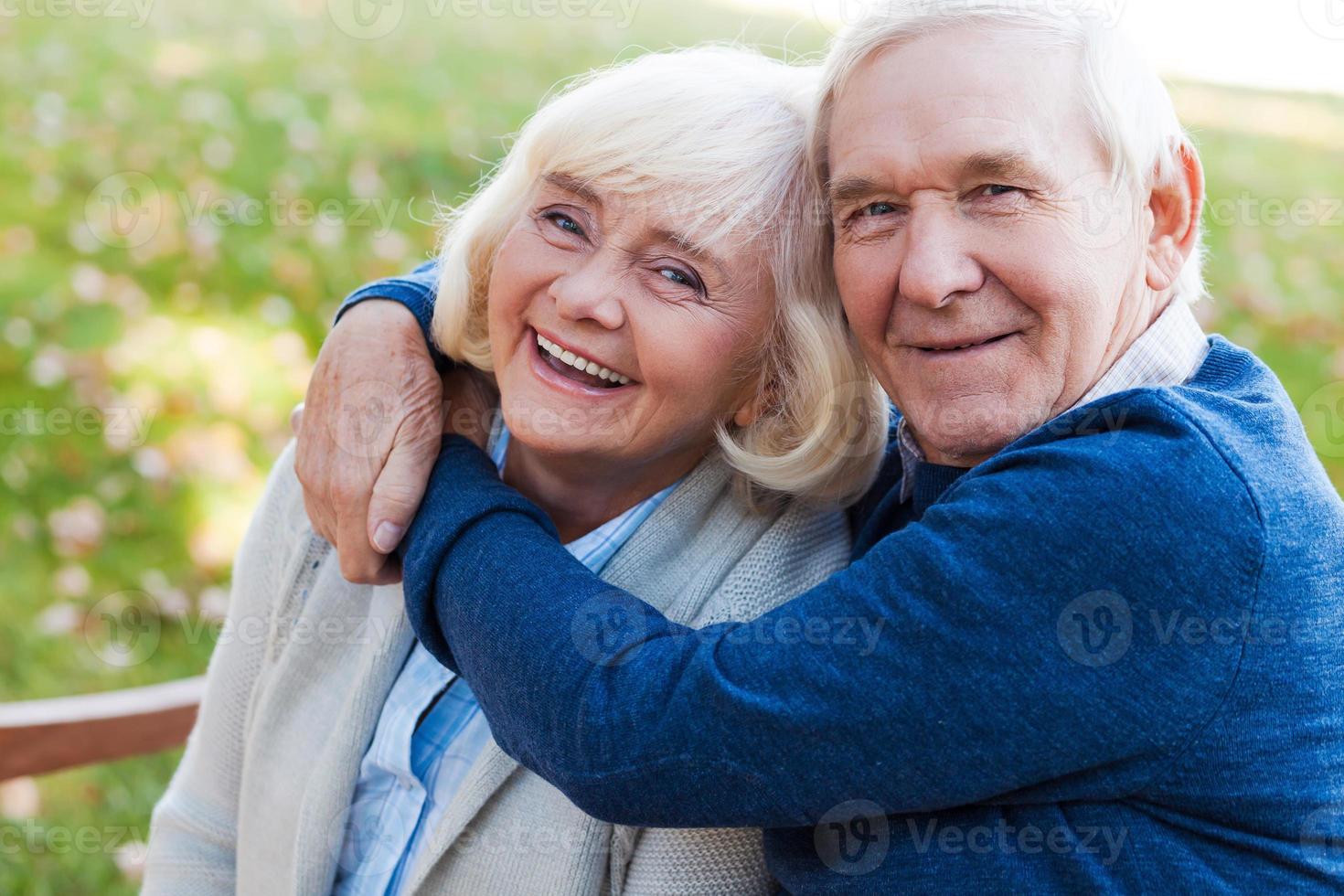 que el amor dure para siempre. feliz pareja de ancianos uniéndose entre sí y sonriendo mientras se sientan juntos en el banco del parque foto