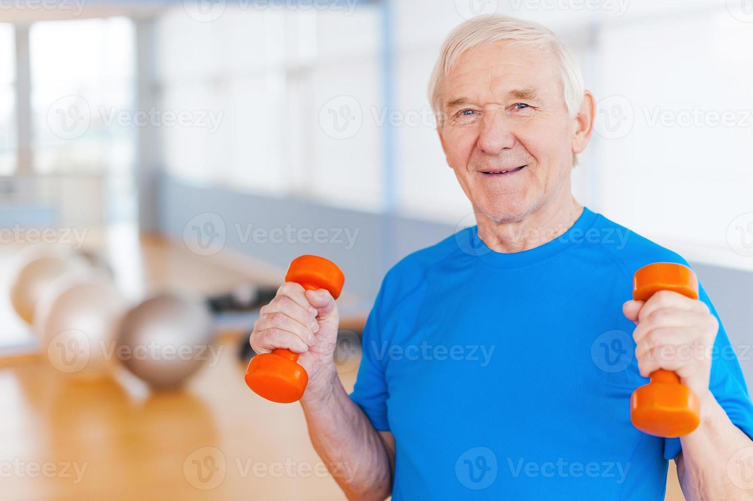 en el camino de la recuperación. feliz anciano haciendo ejercicio con pesas y sonriendo mientras está de pie en el interior foto