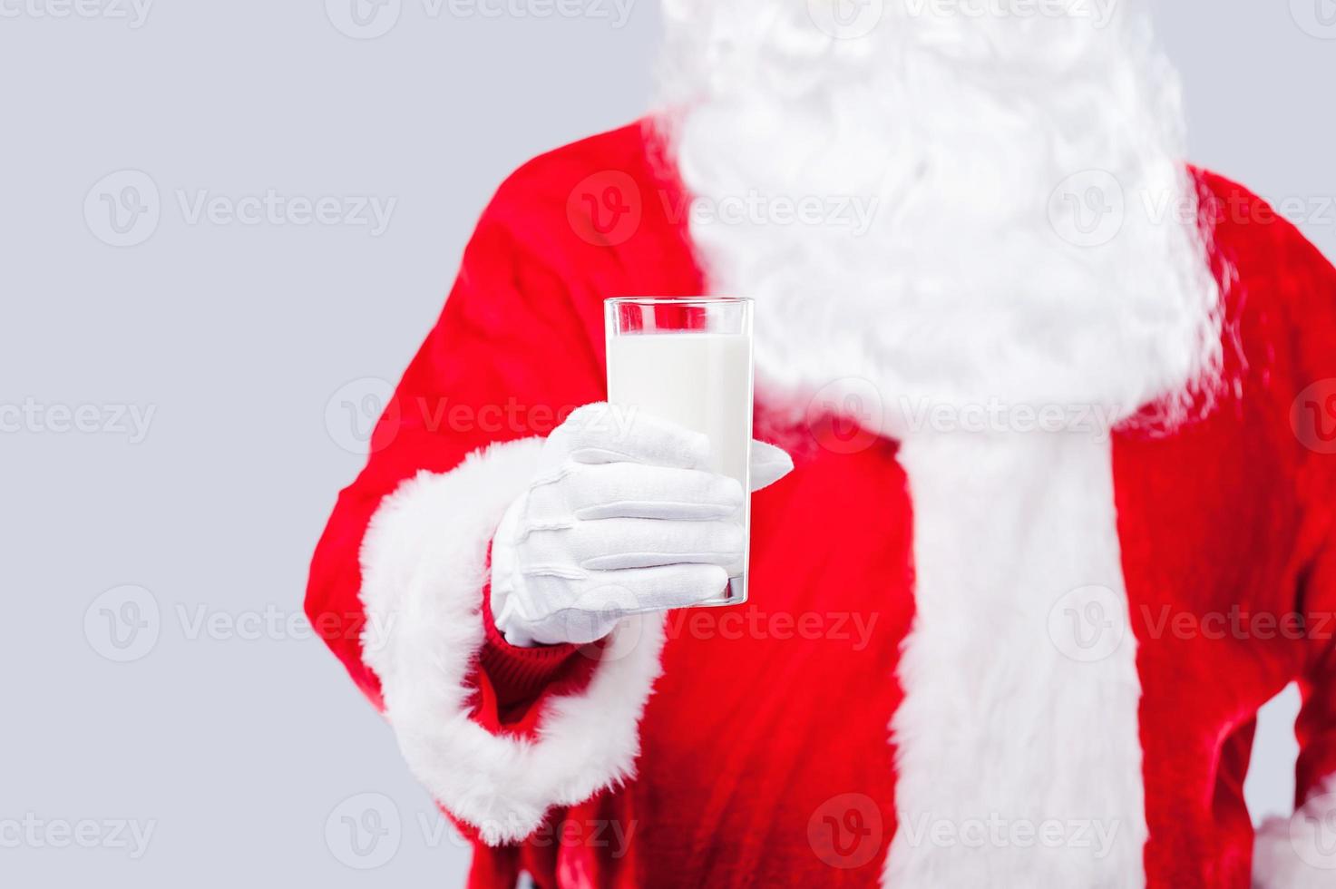 Drink fresh milk Traditional Santa Claus stretching out hand with glass of milk while standing against grey background photo