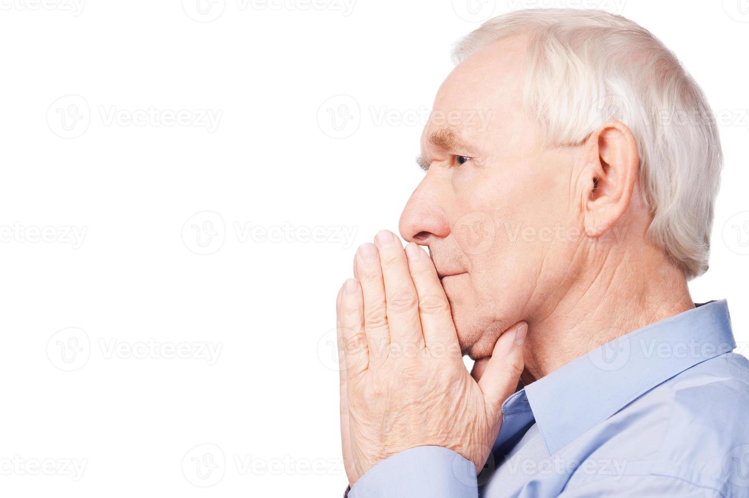 Wise and confident. Side view of senior man shirt holding hands clasped and looking away while sitting in chair at his apartment photo