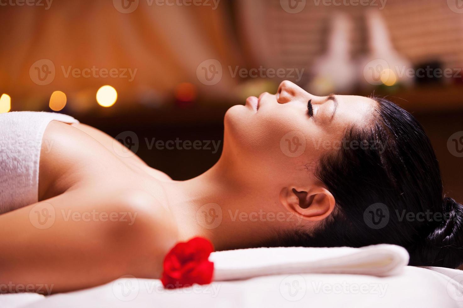 Total relaxation. Side view of beautiful young woman wrapped in towel lying on massage table and keeping eyes close photo