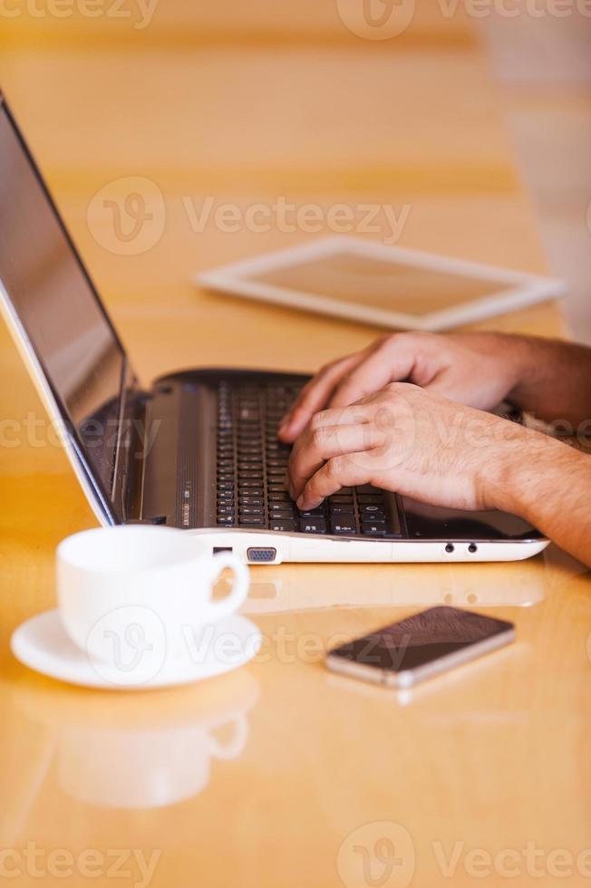 Working in coffee shop. Side view cropped image of thoughtful young man working on laptop while sitting in coffee shop photo