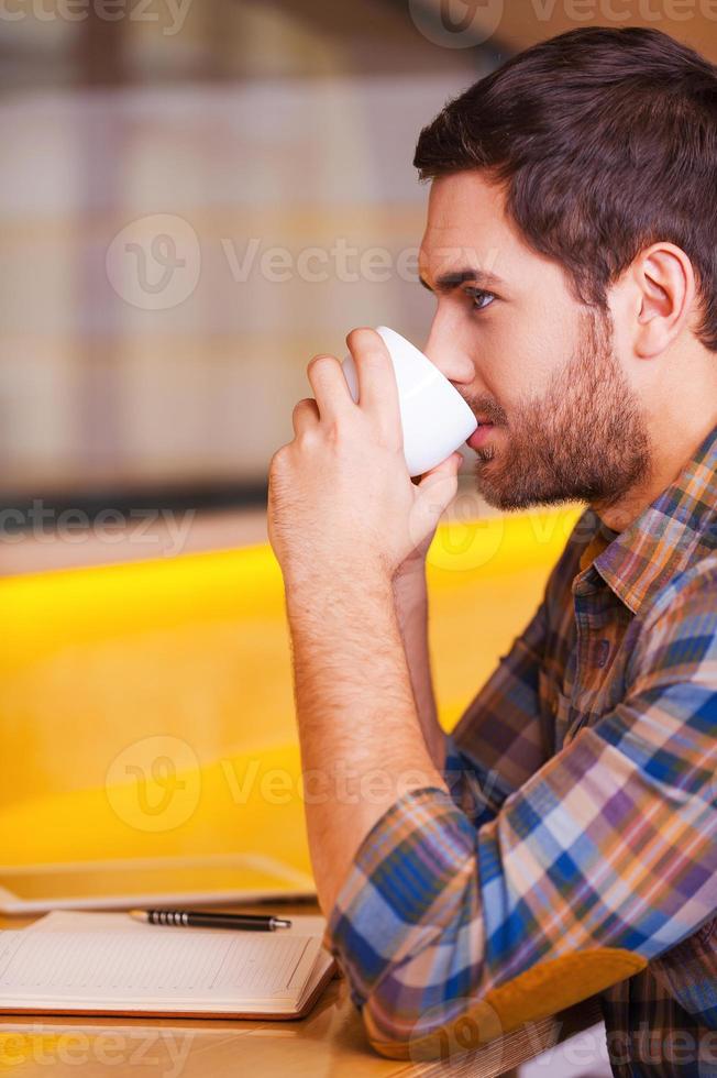 esperando inspiración. vista lateral de un apuesto joven bebiendo café mientras está sentado en una cafetería foto