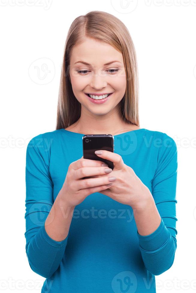 Typing a message to you. Young women holding the mobile phone and smiling while standing against white background photo