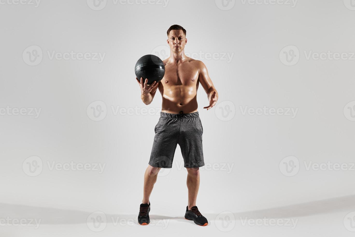 Confident young man with perfect body holding medicine ball against white background photo