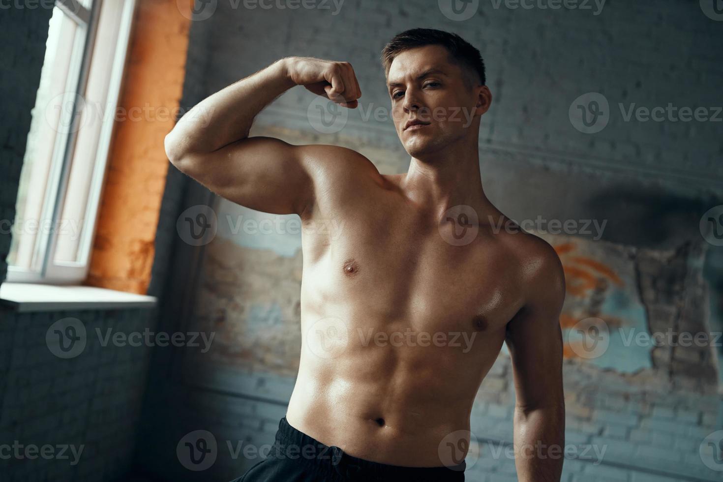 hombre musculoso confiado mostrando su bíceps perfecto mientras está de pie en el gimnasio foto