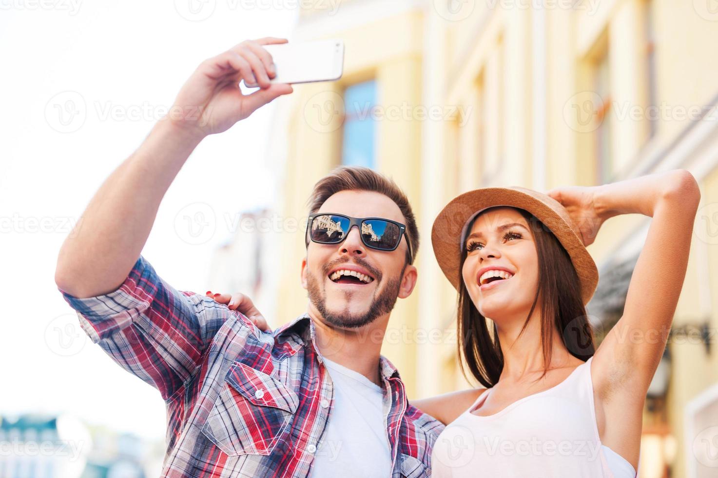 nos encanta hacer selfies. vista de ángulo bajo de la feliz pareja amorosa joven haciendo selfie mientras está de pie juntos al aire libre foto