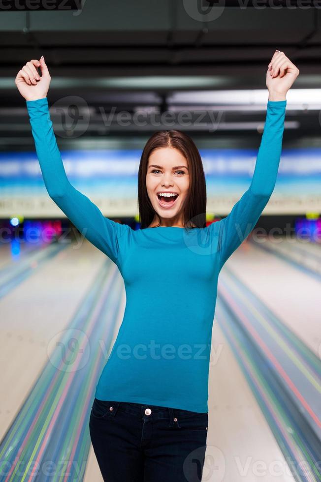 This is strike Beautiful young women keeping arms raised while standing against bowling alleys photo