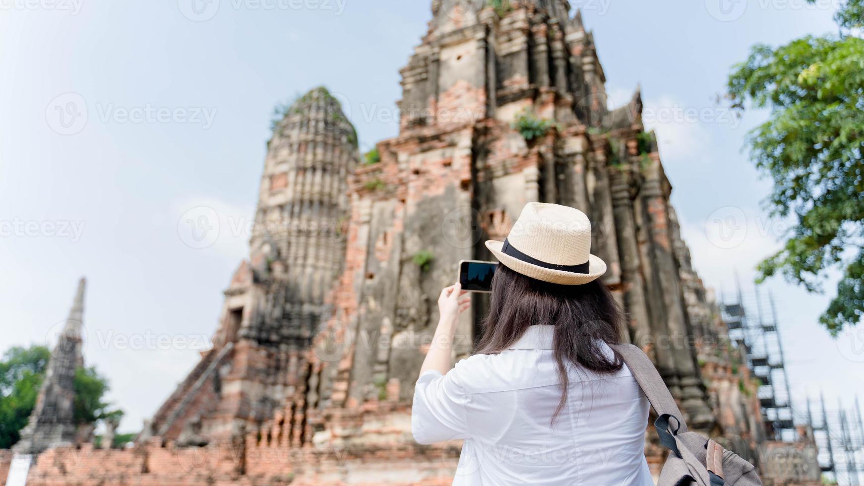 Young asian woman taking photo on his mobile phone camera of a beautiful landscape while standing near temple