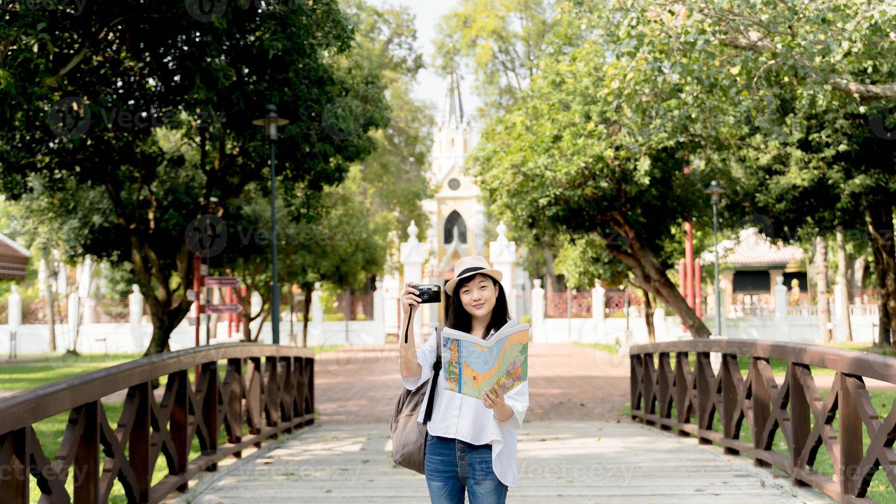 Young Asian woman traveler holding photo camera and map on bridge background