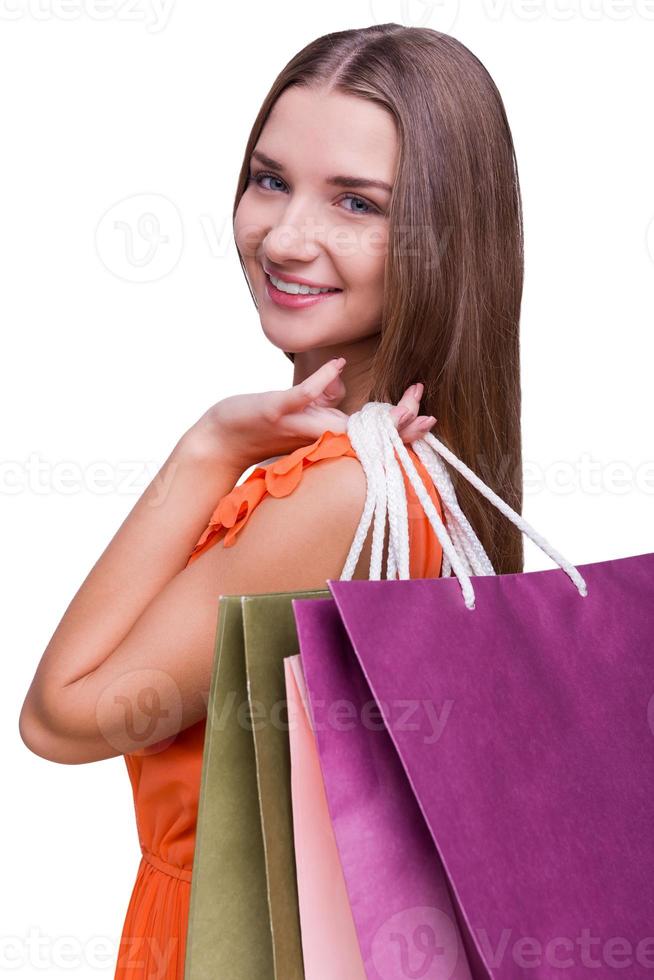 Beautiful shopaholic. Portrait of a beautiful young woman looking over shoulders and holding shopping bags while standing against white background photo
