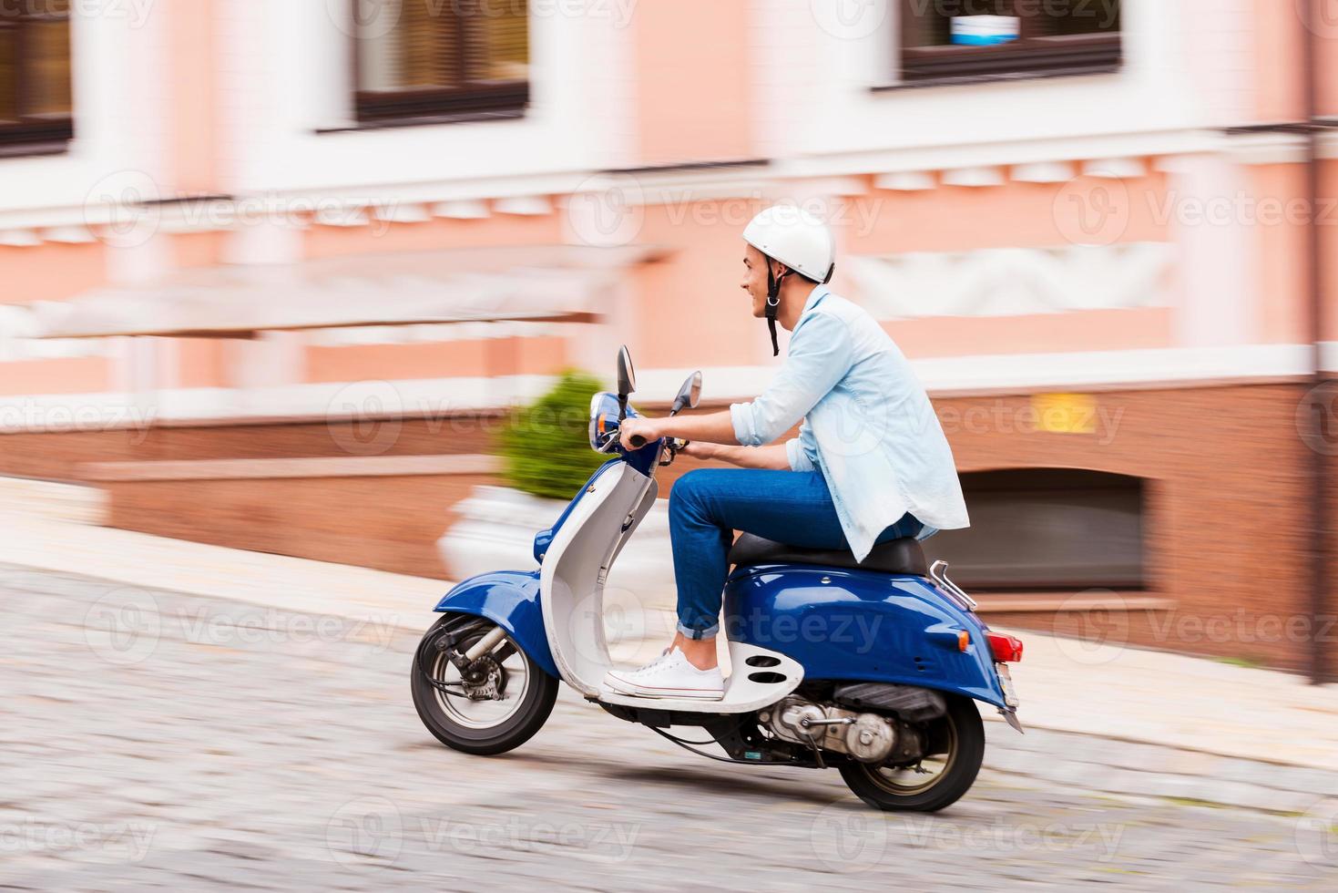 Enjoying his scooter ride. Side view of young man in helmet riding scooter along the street photo