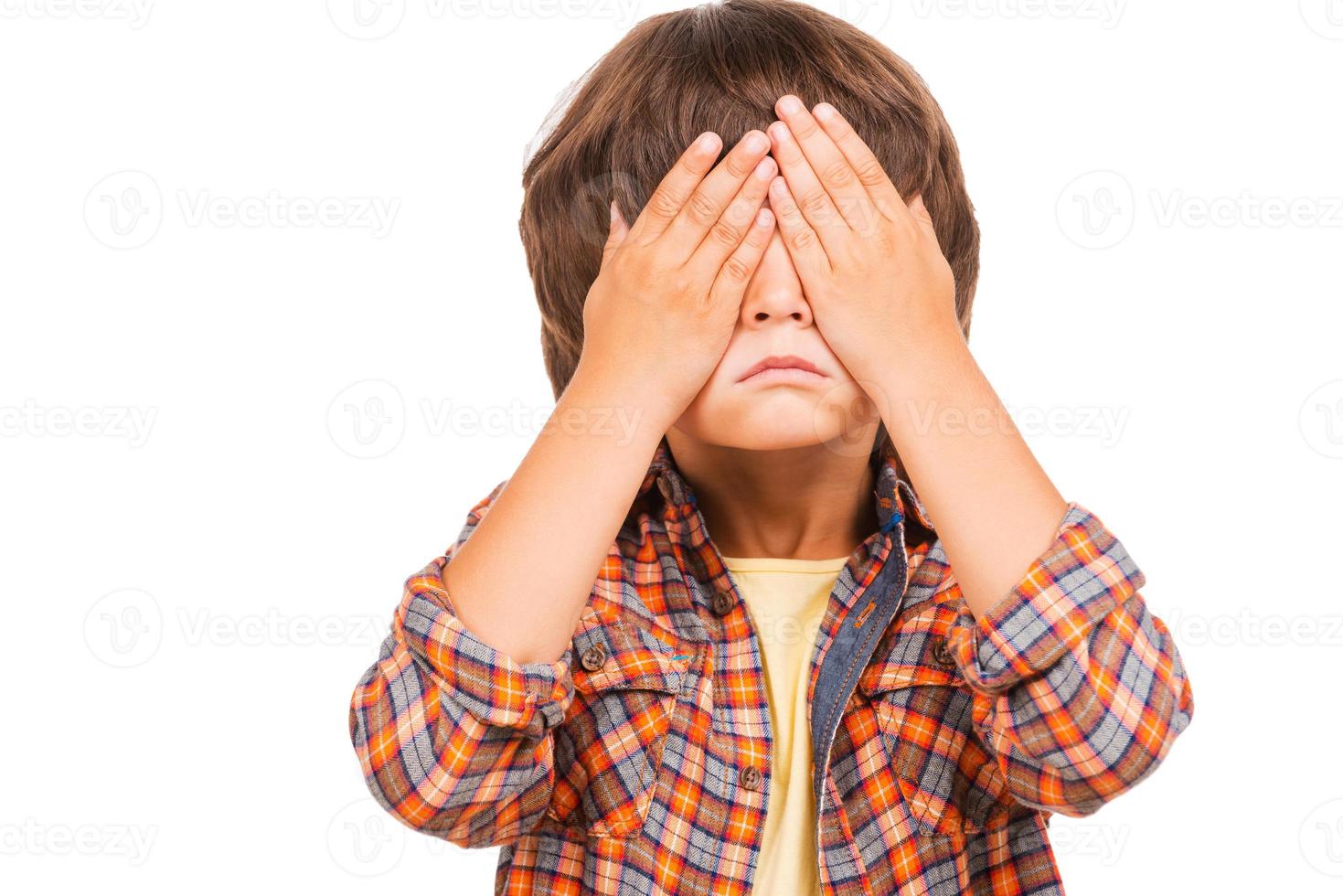 no puedo ver nada lindo niño pequeño cubriendo los ojos con las manos mientras está de pie aislado en blanco foto