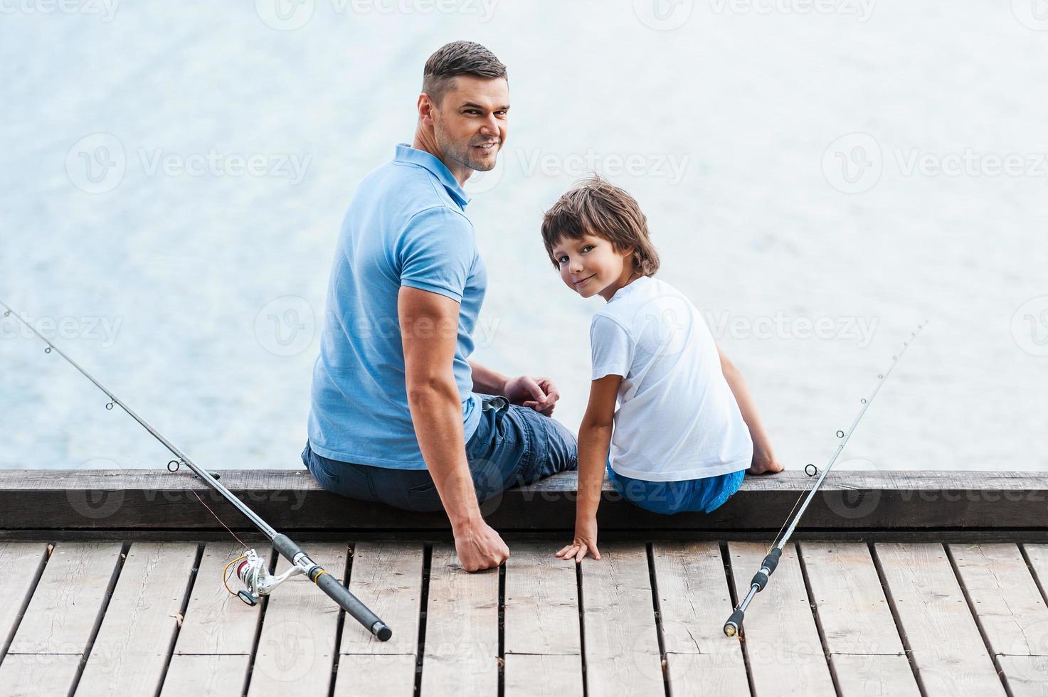 Great day for fishing. Rear view of father and son sitting at the quayside  and looking over shoulder while fishing rods laying near them 13288771  Stock Photo at Vecteezy