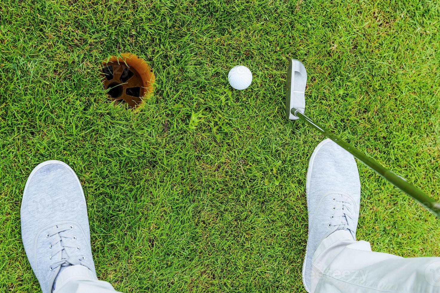 One shot to success. Top view of golfer putting while standing on green and near the hole photo