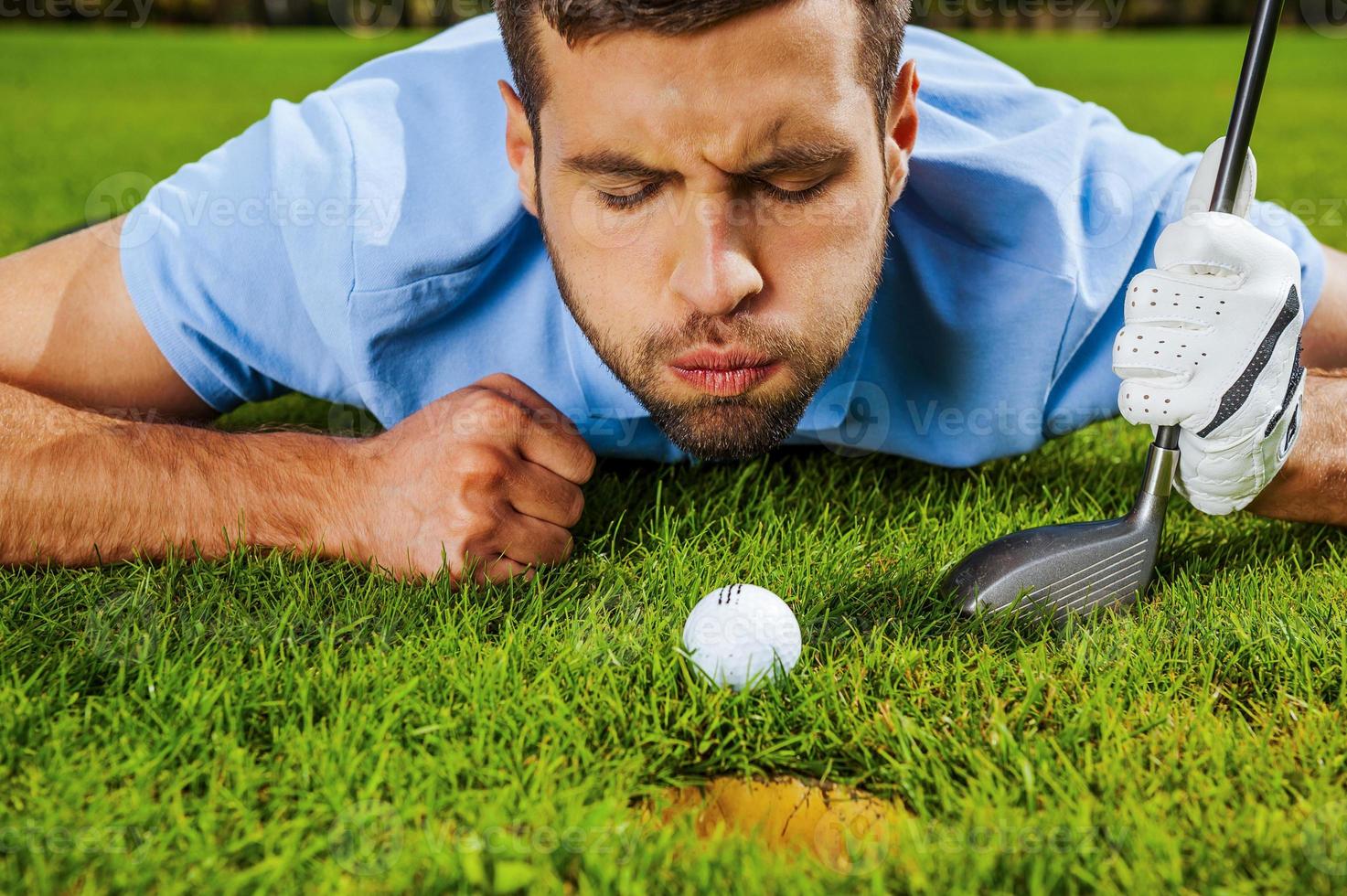 Almost in. Close-up of young golfer blowing at the ball while lying near the hole photo