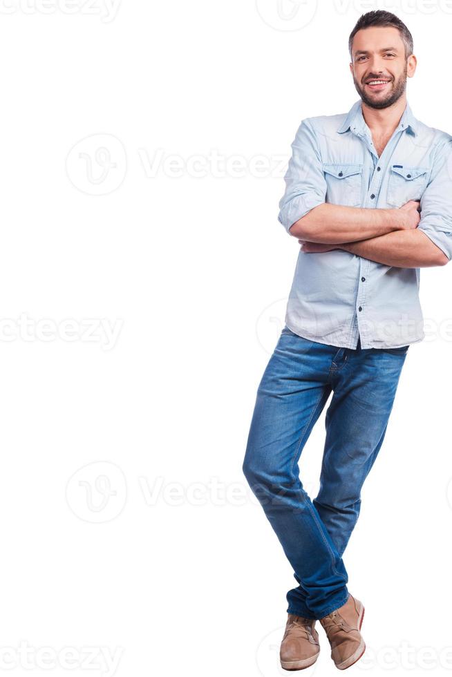 Casually handsome. Full length of handsome young man in casual wear leaning at copy space and smiling while standing against white background photo