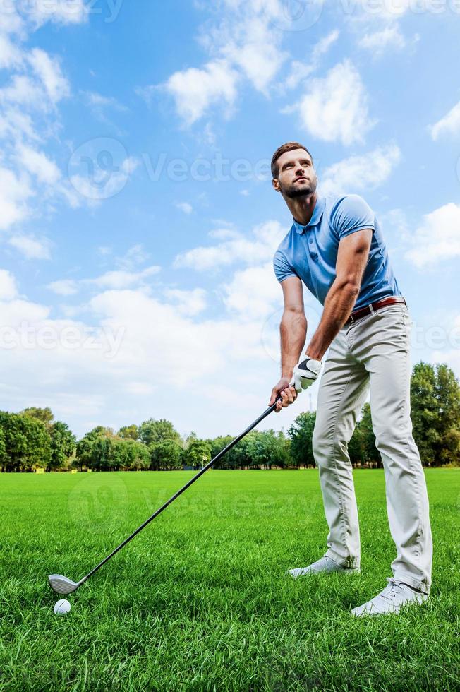 Ready to strike. Low angle view of young man playing golf while standing on green photo