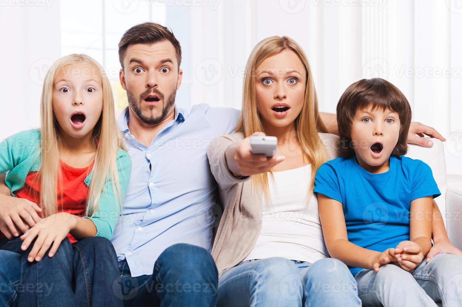 eso es una familia asombrosamente sorprendida de cuatro personas que se unen entre sí y mantienen la boca abierta mientras miran televisión juntos en casa foto