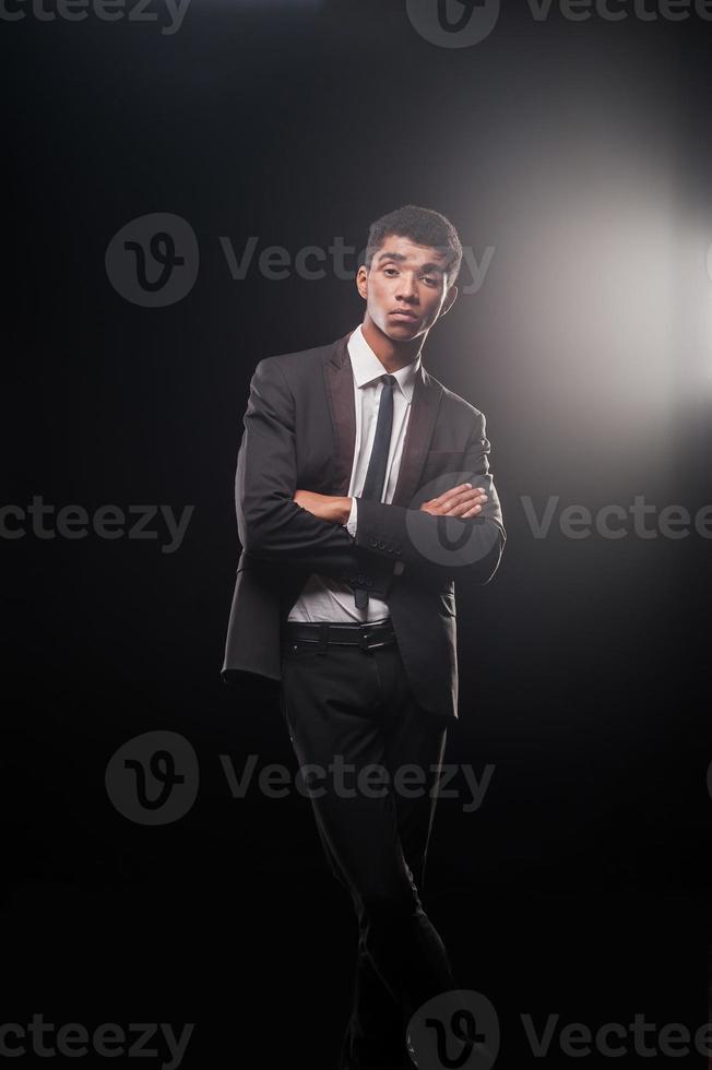 teniendo éxito satisfaciendo él. apuesto joven afroamericano manteniendo los brazos y las piernas cruzadas foto