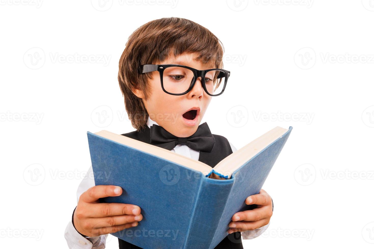 No way Wide angle image of surprised little boy reading book and keeping mouth open while standing isolated on white photo