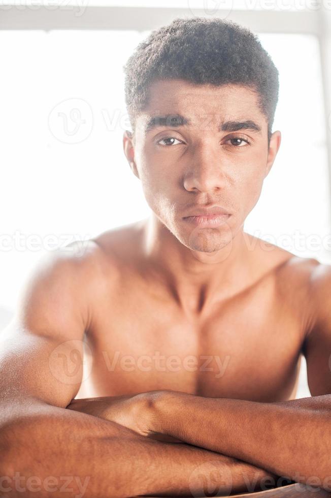 Young and brutal. Handsome young  Afro-American man sitting on the chair and looking at camera photo