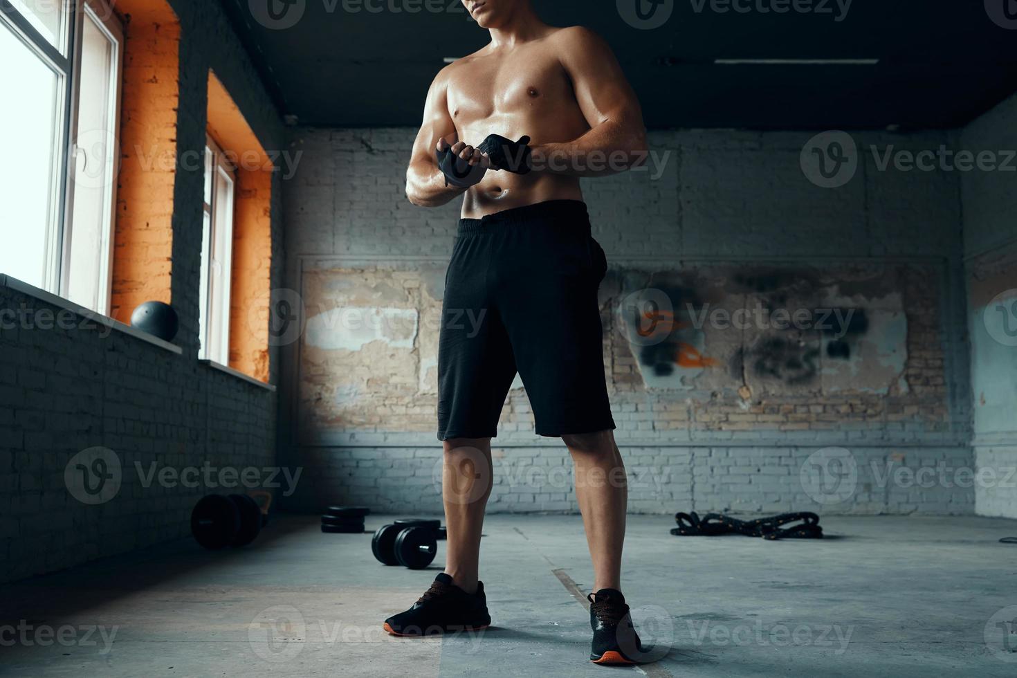 hombre musculoso irreconocible con guantes deportivos mientras está de pie en el gimnasio foto