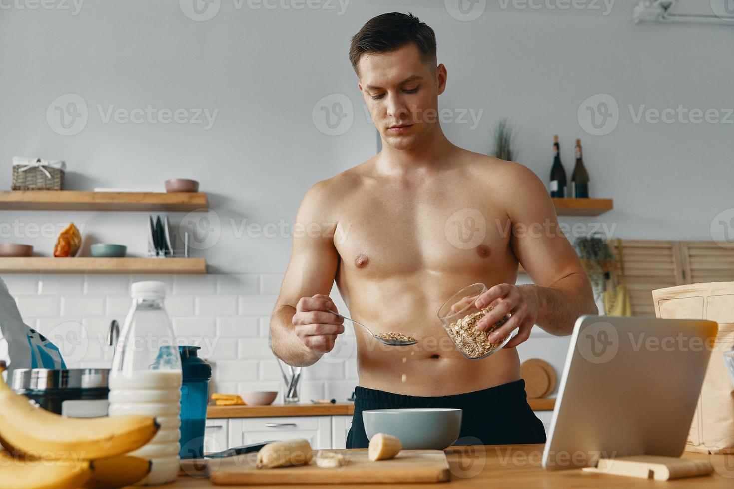 Handsome fit man preparing healthy food while standing at the kitchen photo
