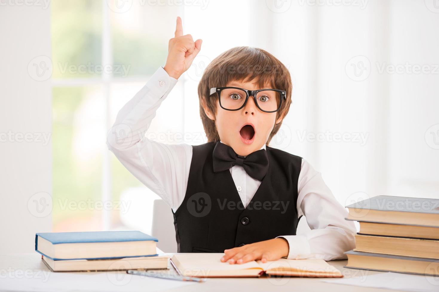 niño feliz sosteniendo un libro y gesticulando mientras está sentado en la mesa foto