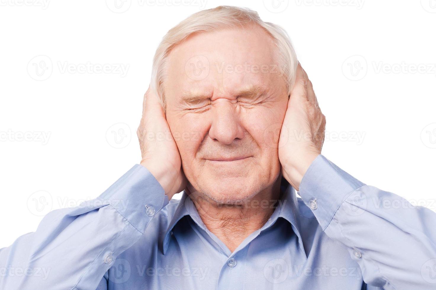 This is too loud Frustrated senior man in shirt holding head in hands and keeping eyes closed while standing against white background photo