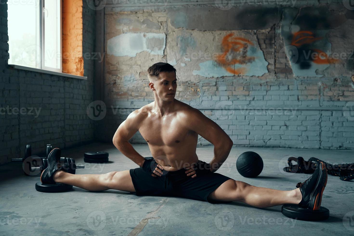 Fit young man holding hands on hip while doing the splits in gym photo