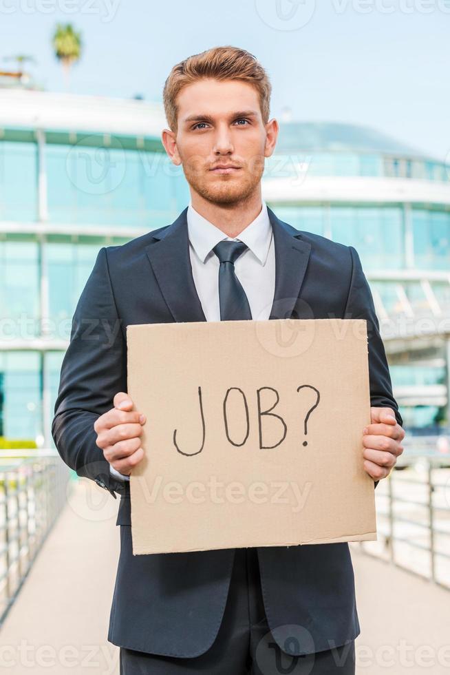 I need a job Handsome young man in formalwear holding poster with job text message while standing outdoors and against building structure photo