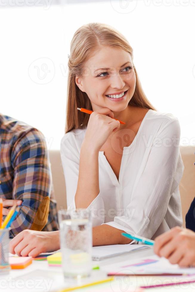 Working with pleasure. Confident young woman in smart casual wear looking away and smiling while sitting at her working place photo