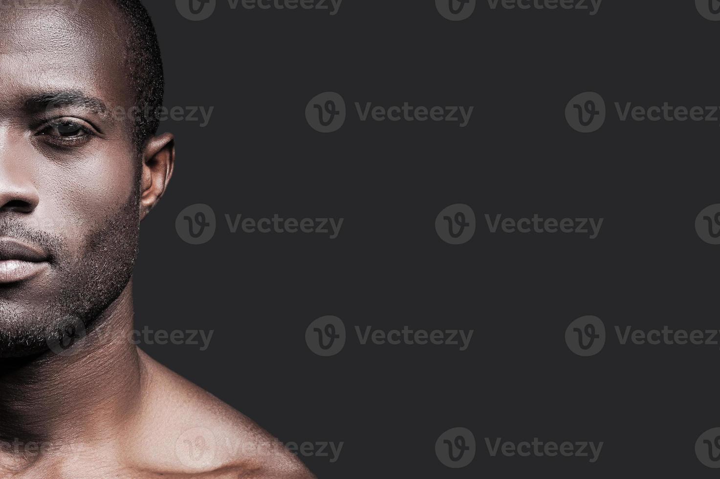 Confident and handsome. Half face of confident young African man looking at camera while standing against grey background photo