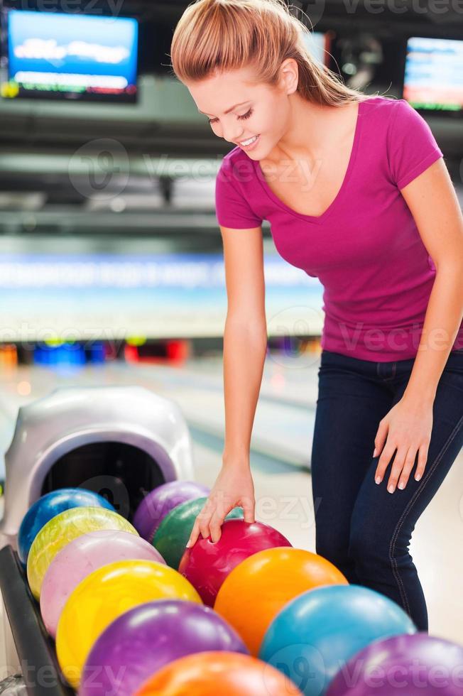 I choose my favorite color. Cheerful young women choosing bowling ball and smiling while standing against bowling alleys photo