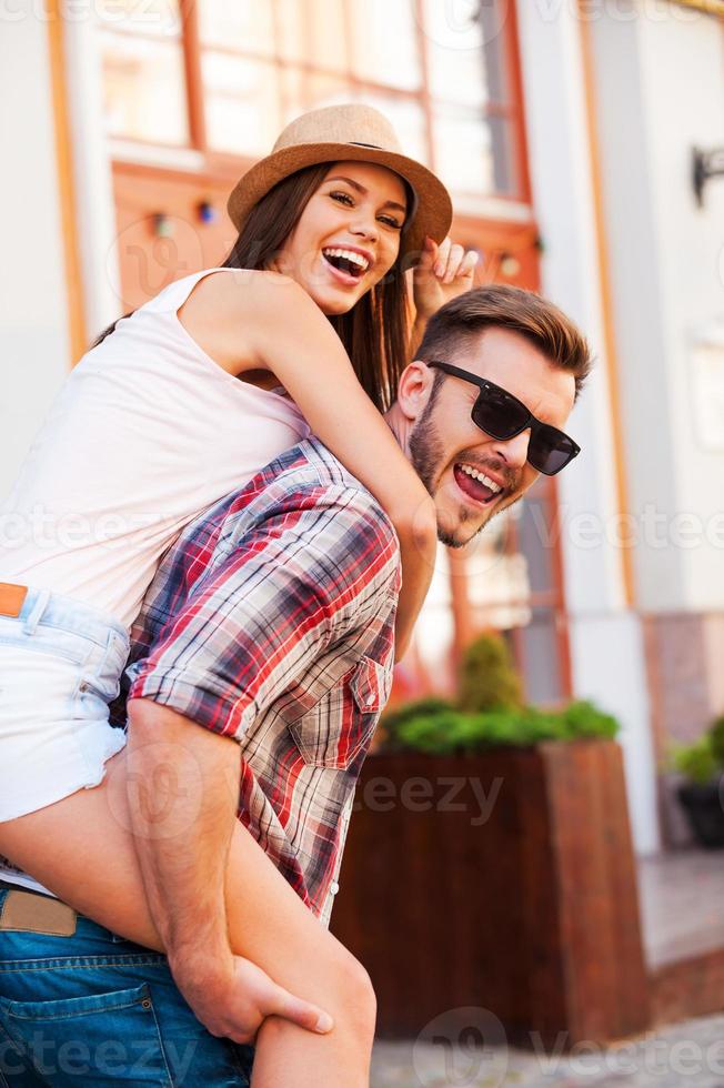 disfrutando de su tiempo libre juntos. joven feliz cargando a su hermosa novia sobre los hombros y mirando a la cámara mientras camina por la calle foto