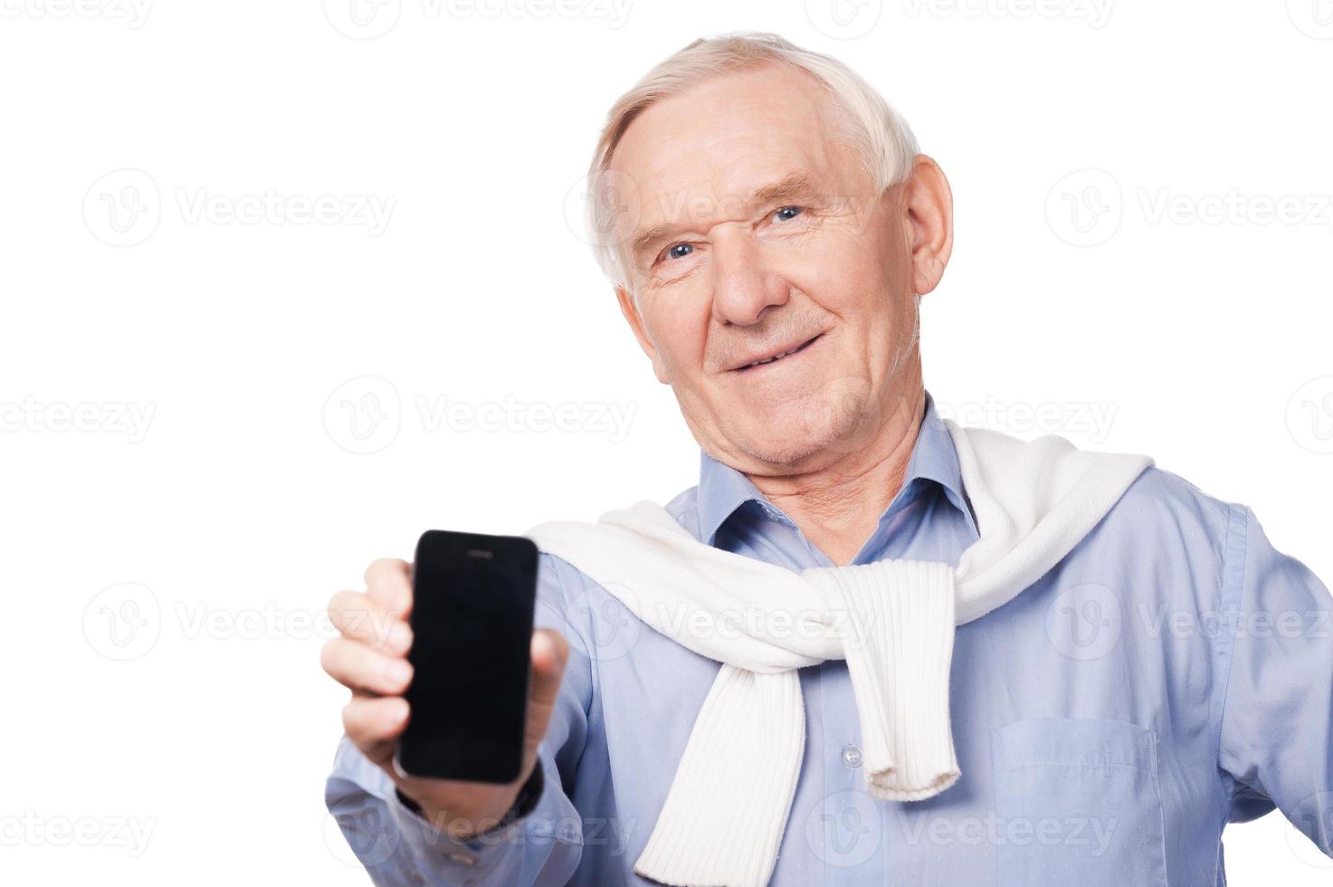 Copy space on my telephone. Portrait of happy senior man showing his mobile phone while standing against white background photo