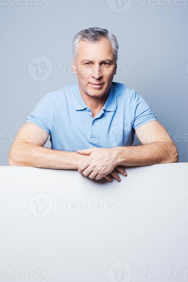 Under copy space. Handsome senior man leaning at copy space while standing against grey background photo