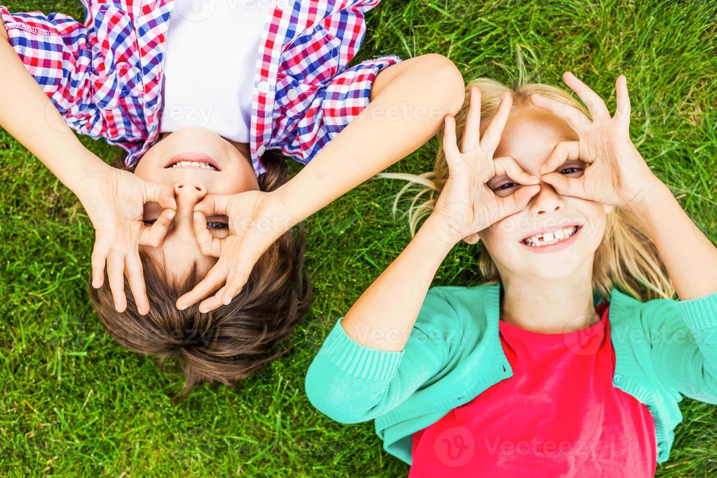 Summer fun. Top view of two cute little children making faces and smiling while lying on the green grass together photo