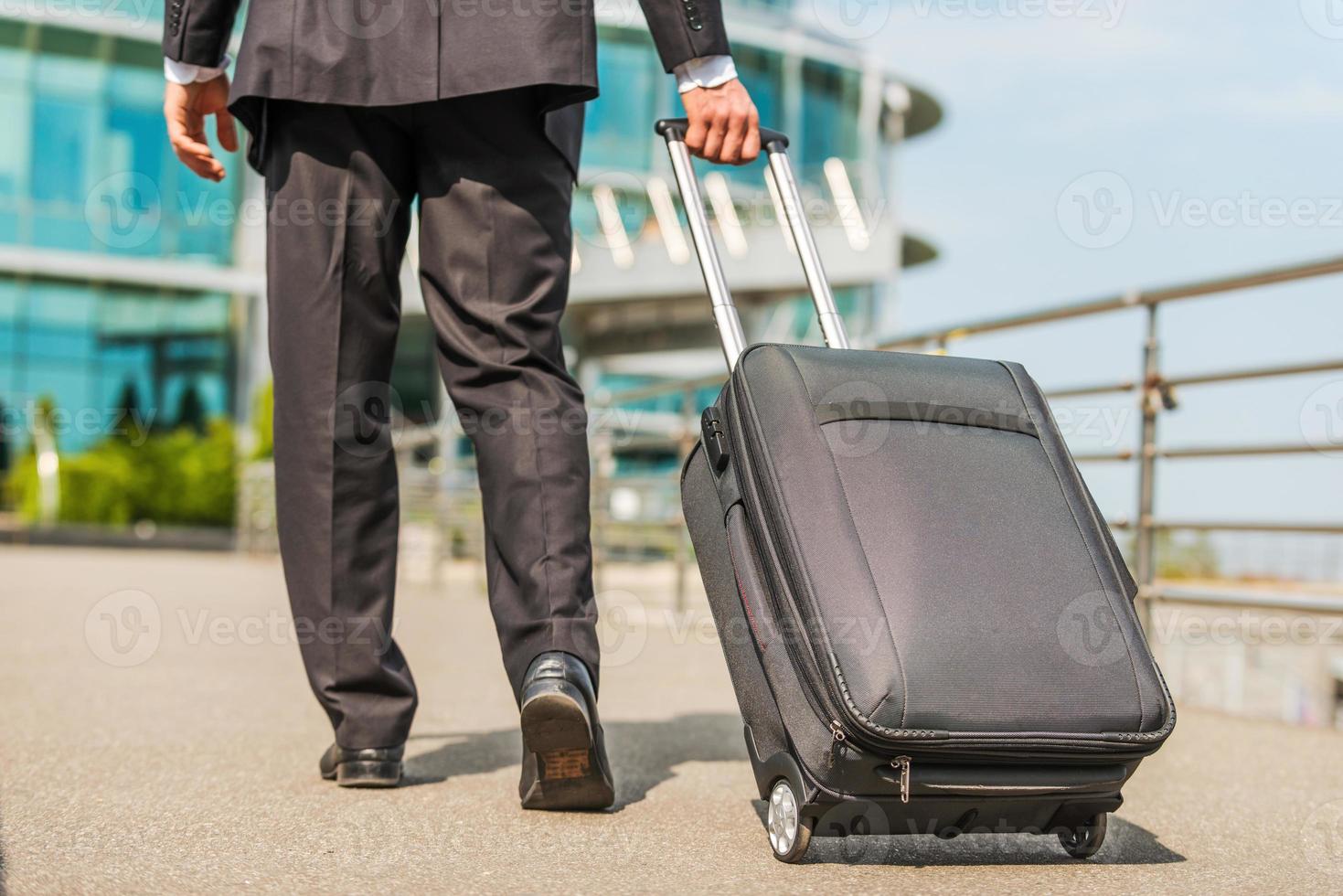 Ready to business trip. Rear view of businessman in formalwear carrying suitcase while walking away photo
