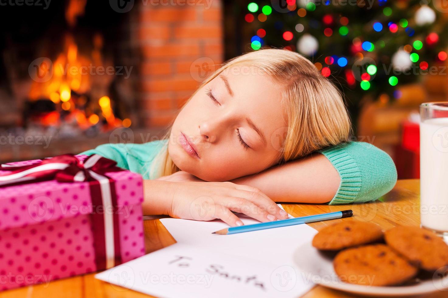 Little daydreamer. Cute little girl sleeping while leaning her head at the table with Christmas tree and fireplace in the background photo