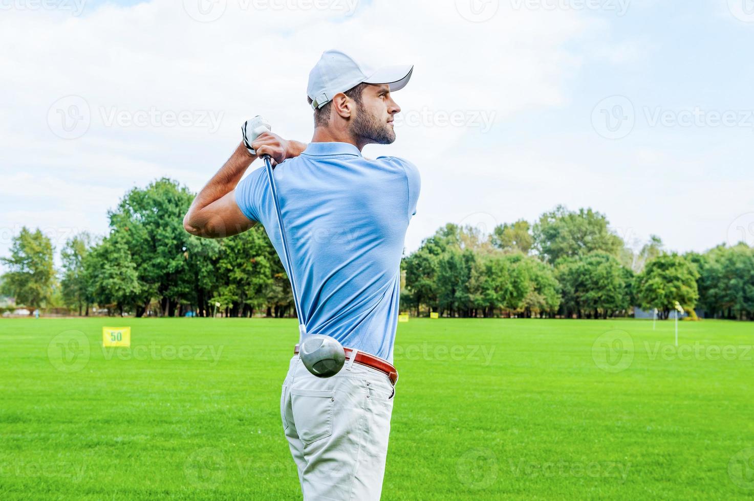 Great strike. Side view of confident golfer swinging his driver and looking away while standing on golf course photo