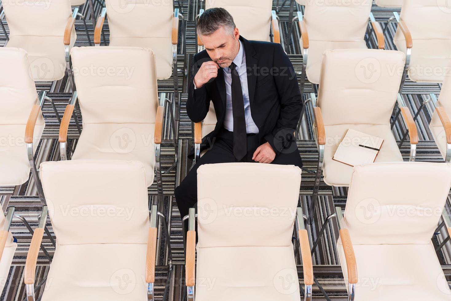 The one and only. Top view of bored mature man in formalwear sitting on the chair in empty conference hall photo
