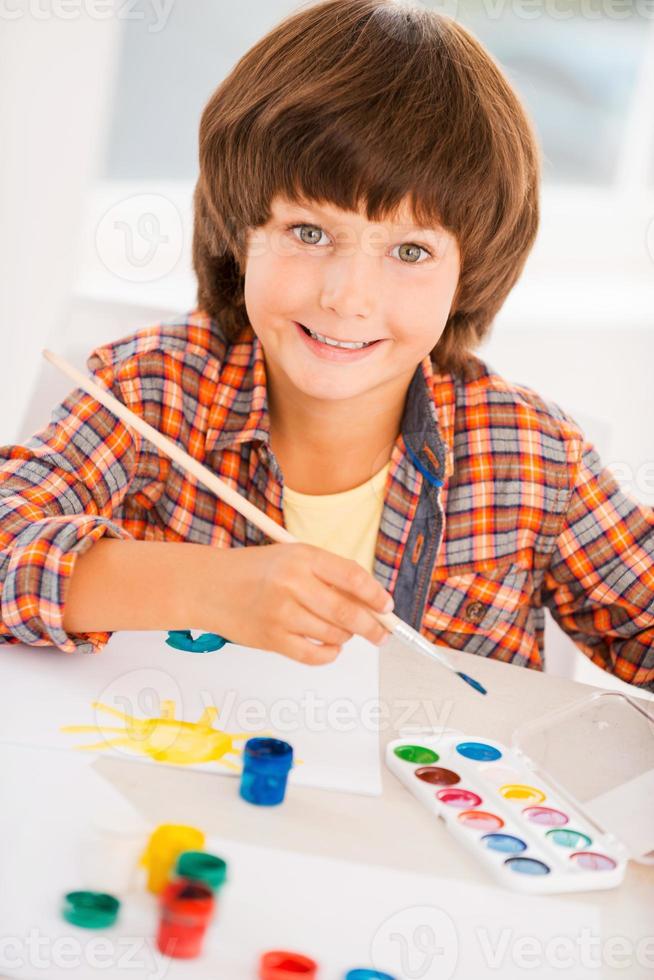 Painting is fun. Top view of little boy relaxing while painting with watercolors sitting at the table photo