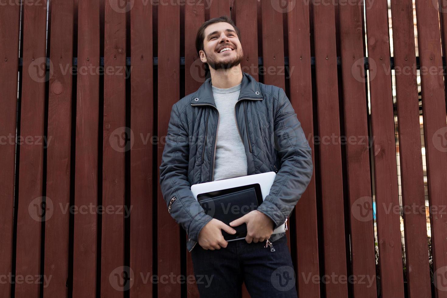 happy man Businessman with a laptop in his hands looks dreamily up on the background of wooden structures photo