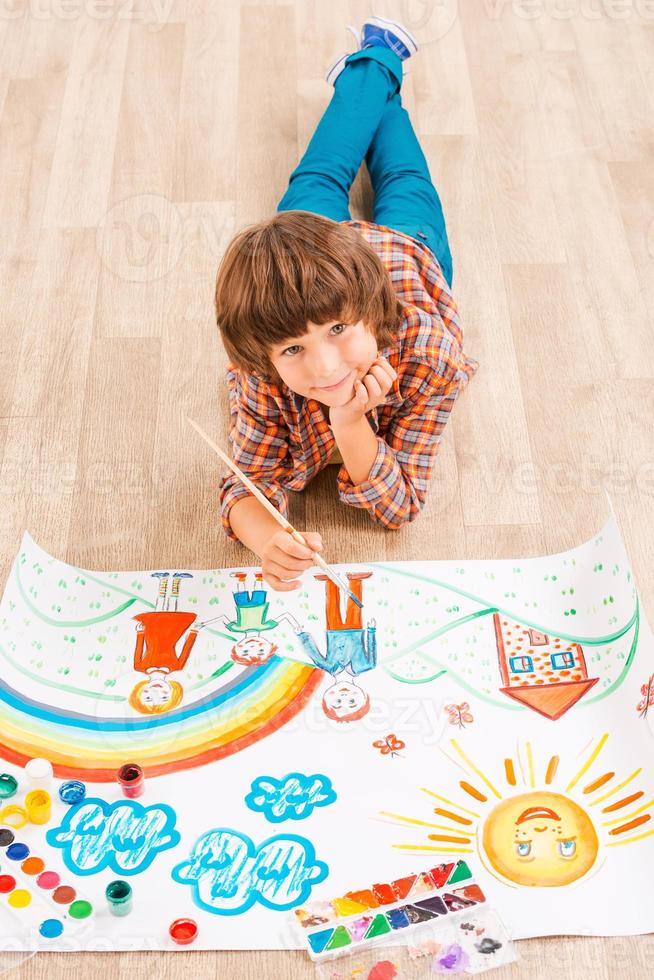 Boy painting. Young boy relaxing while painting with watercolors lying on the floor photo