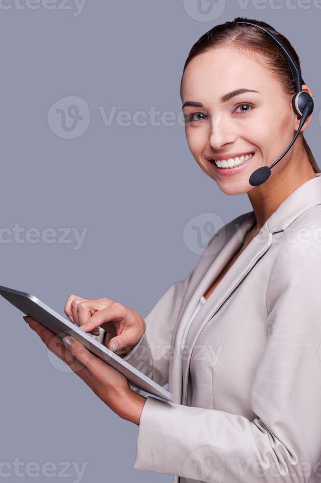 Beauty at work. Side view of Confident young female operator holding digital tablet while standing against grey background photo