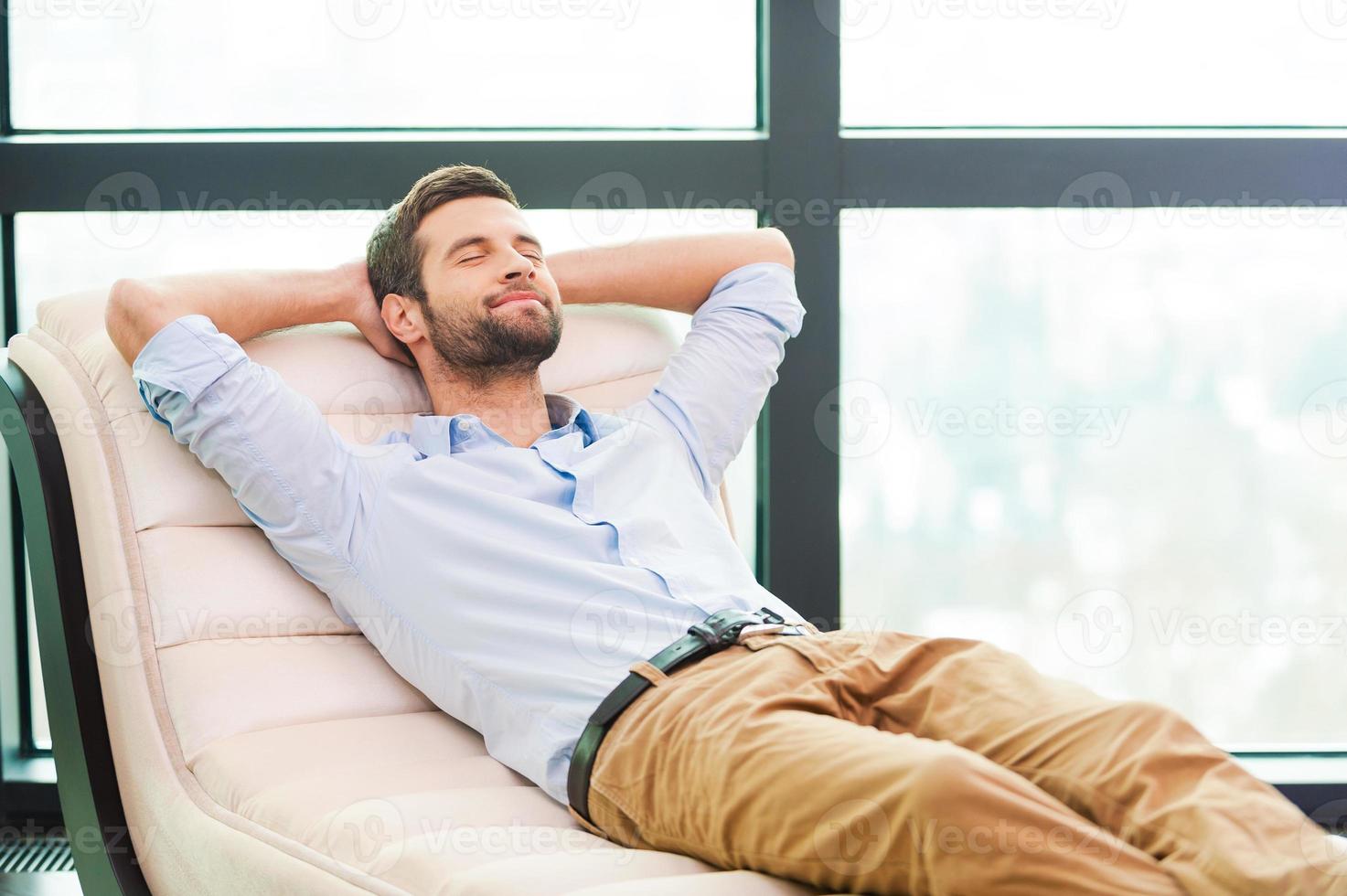 hermoso soñador de día. apuesto joven cogido de la mano detrás de la cabeza mientras duerme en el sofá foto