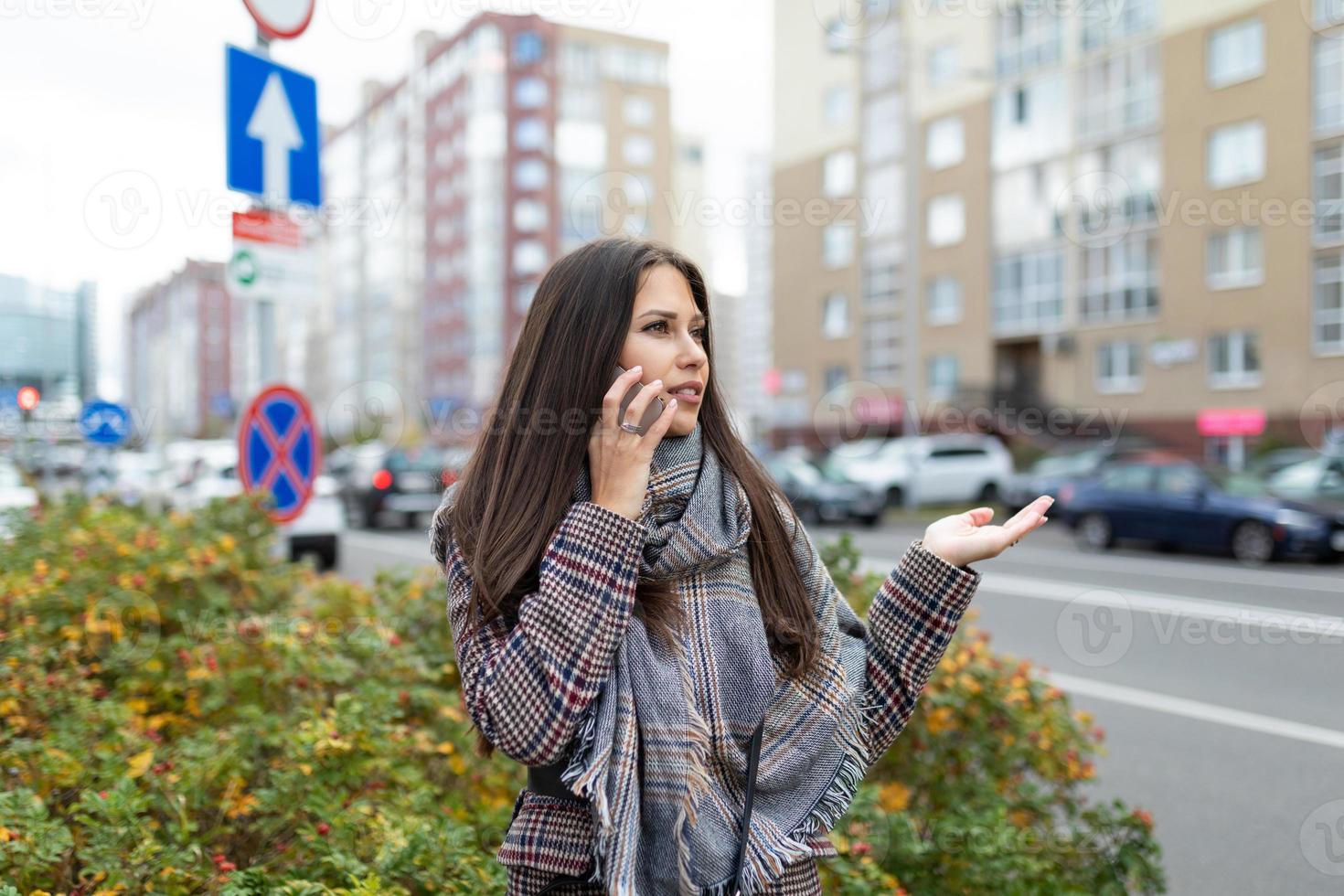 stylish young woman speaks on a mobile phone near the road with gestures shows confusion, catches a taxi photo